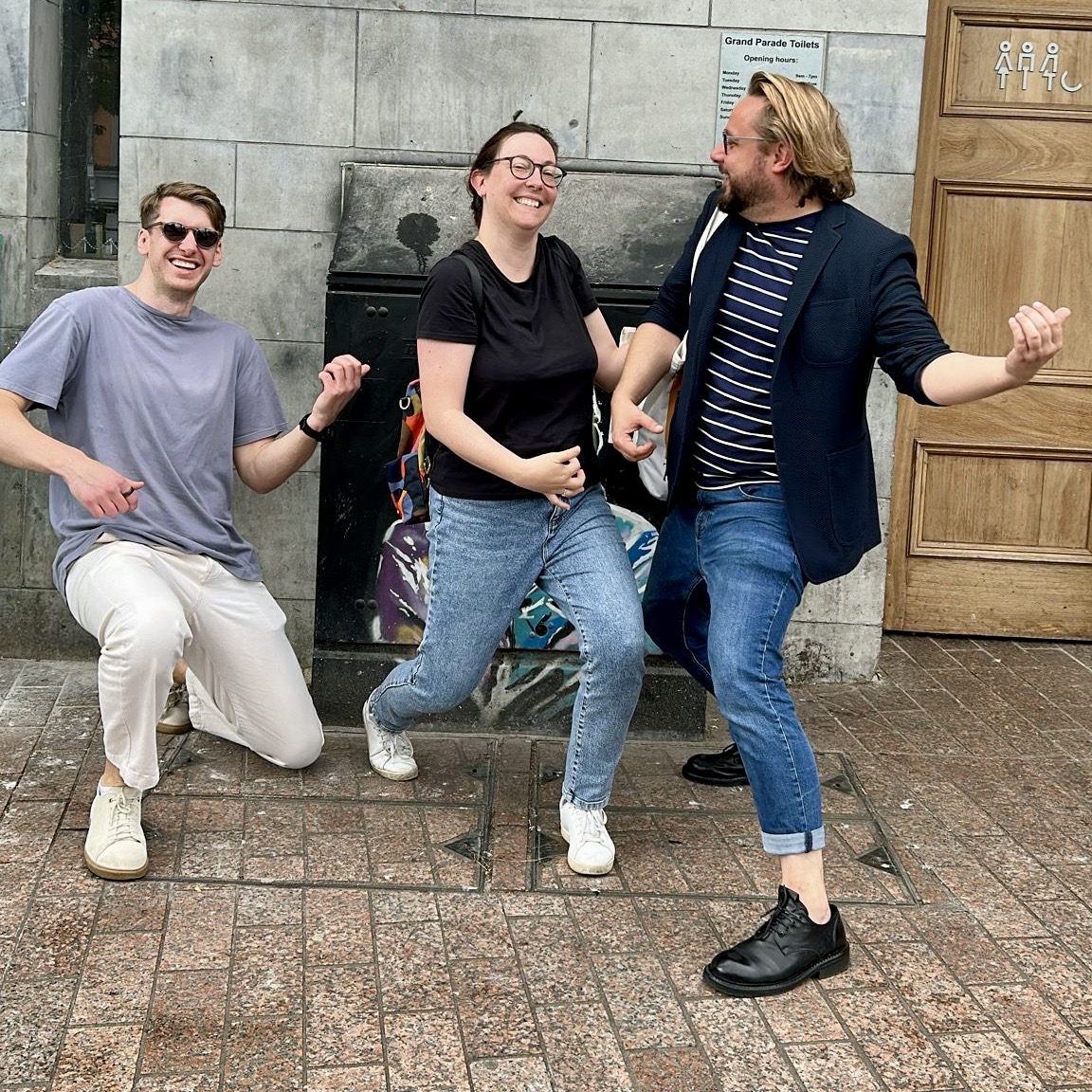 Three scavenger hunt participants laughing while miming a challenge on a Cork city street