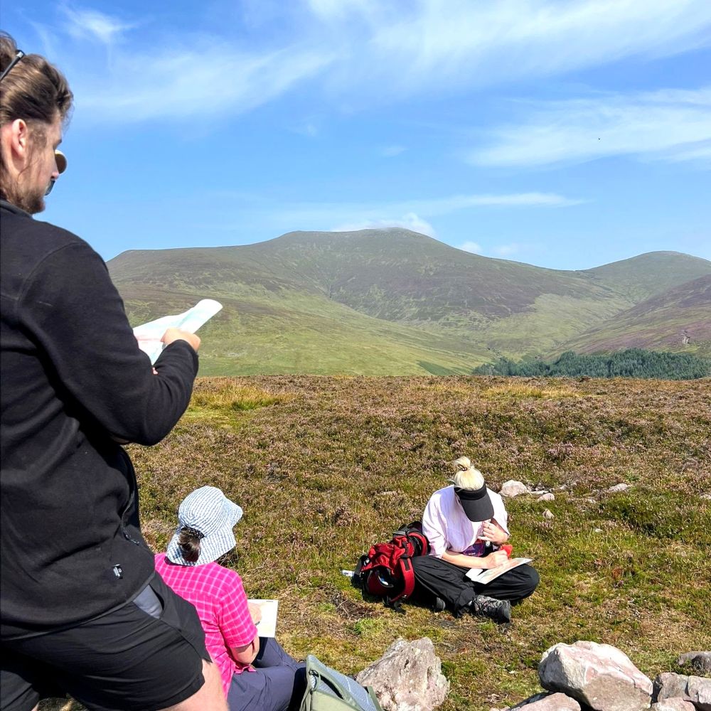 Mountain Skills participants working with maps on a heather hillside